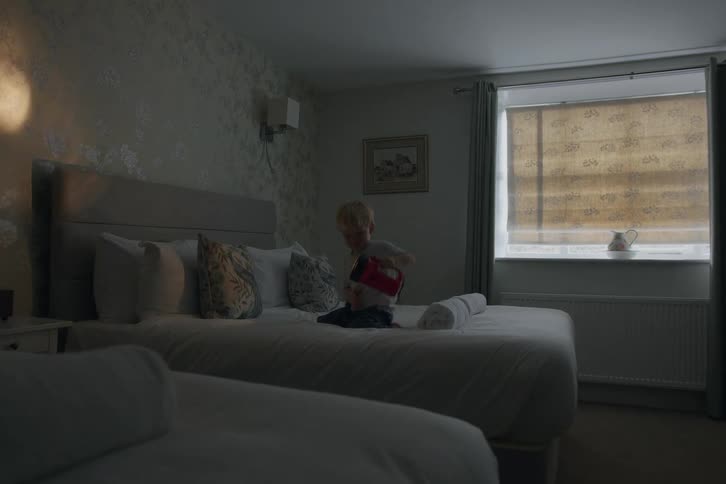 Blonde boy kneeling on bed plays with flashlight