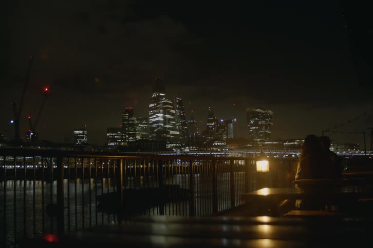 Couple having a date sitting next to the dim light of a lamp while they enjoy the view of the city over the bridge and the river
