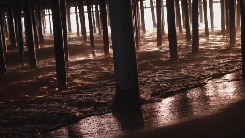 Waves washing ashore under a pier as the sun sets