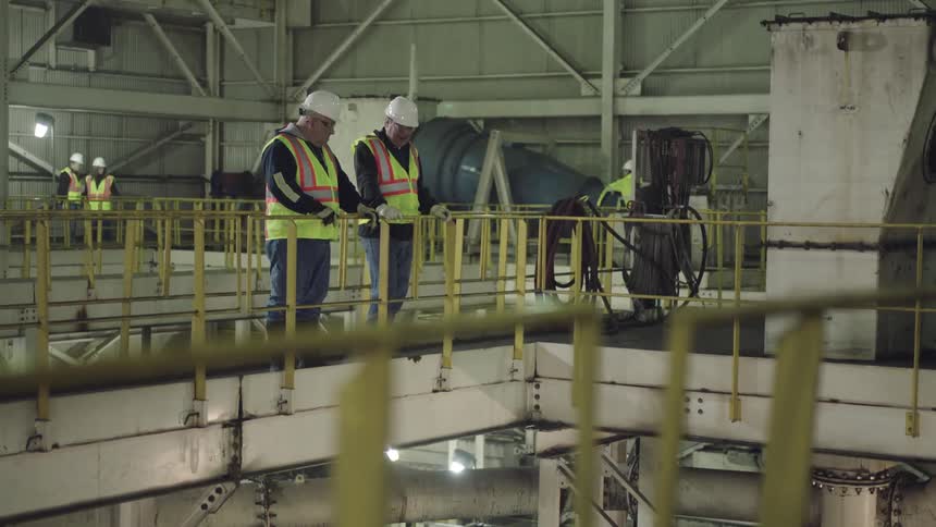 Workers stand on a platform wearing hard hats
