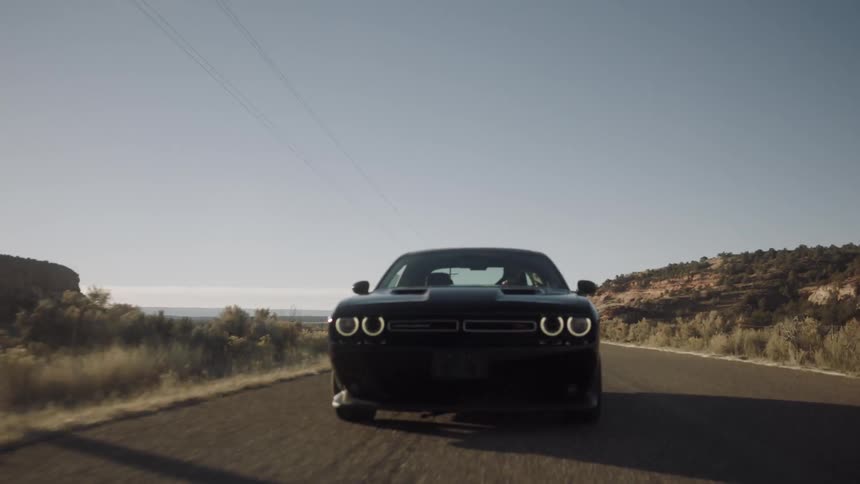 A black car races down a road near the desert