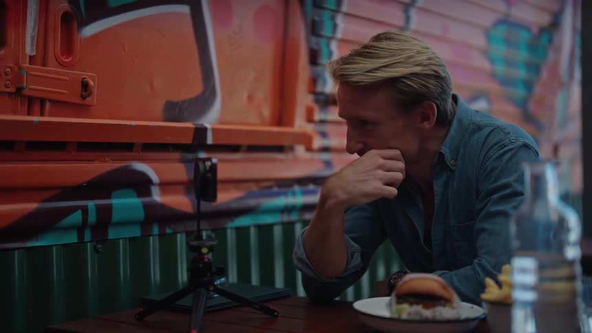 Man in blue shirt sits at table using smartphone next to wall with graffiti