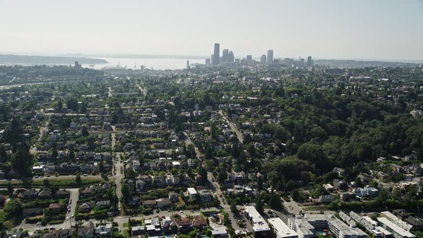  aerial footage capturing the picturesque Seattle skyline with towering buildings and residential neighborhoods overlooking Lake Washington on a sunny day in the Pacific Northwest
