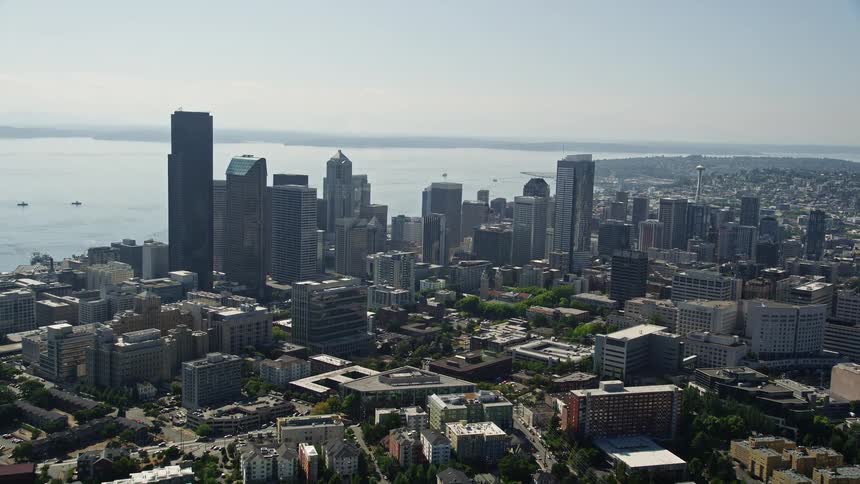 Aerial footage flies over the skyscraper-filled downtown Seattle skyline with the sun shining on a hazy day in Washington State