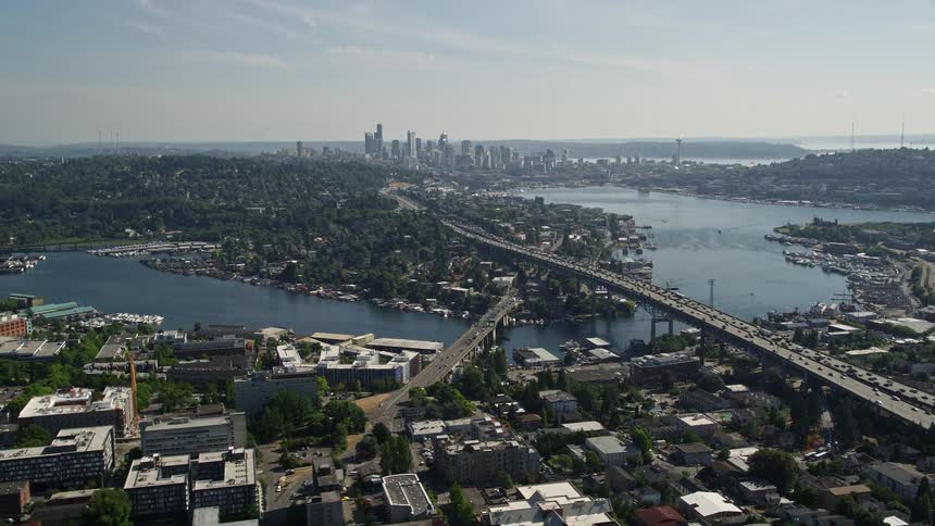 Fly away from Ship Canal Bridge to reveal Lake Union and the stunning skyline of Downtown Seattle Washington showcasing the bustling metropolis beautiful nature and transportation in the sunny daytime
