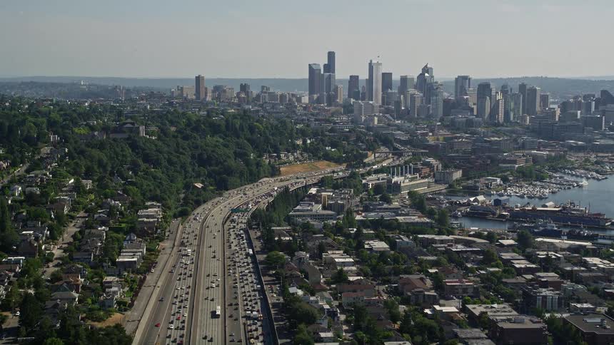 Aerial view of heavy traffic on Interstate 5 approaching the Downtown Seattle skyline revealing a metropolis with high-rise buildings and transportation in the sunny cityscape of Washington