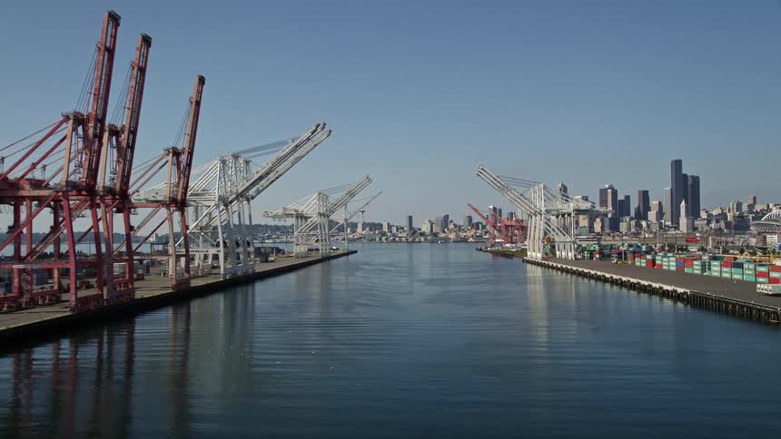 Aerial view of cranes along the shipping docks in a metropolitan city with tall buildings towers on the skyline and a mountainous backdrop