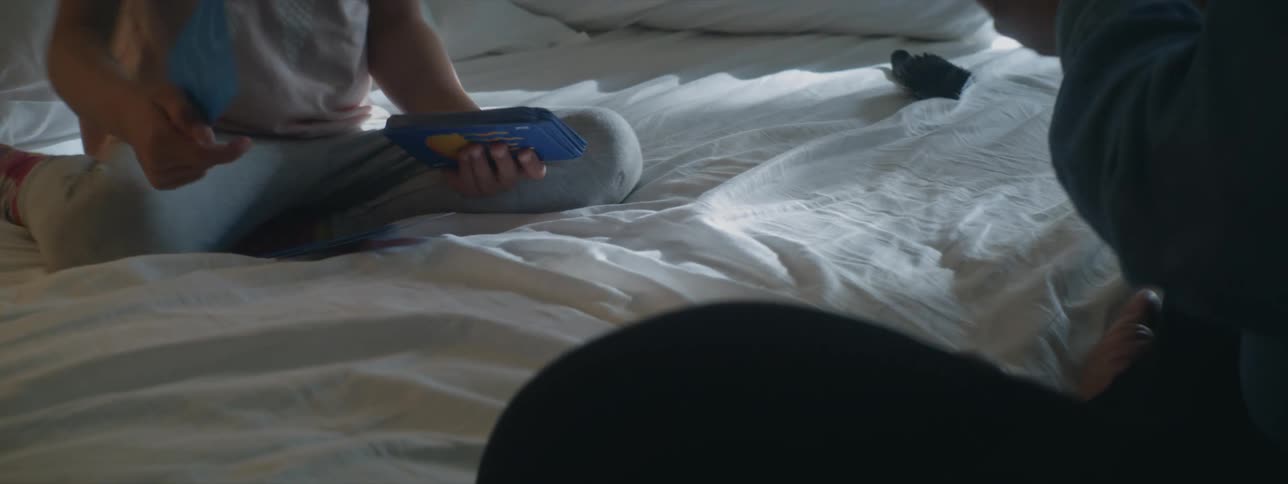 Two individuals engage in a leisurely activity on a bed enjoying a playful moment as they interact and play with cards creating a cozy and enjoyable atmosphere of shared amusement