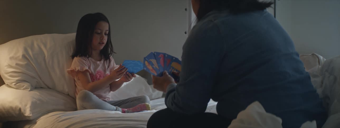 Mother and daughter sit crosslegged on bed playing a card game