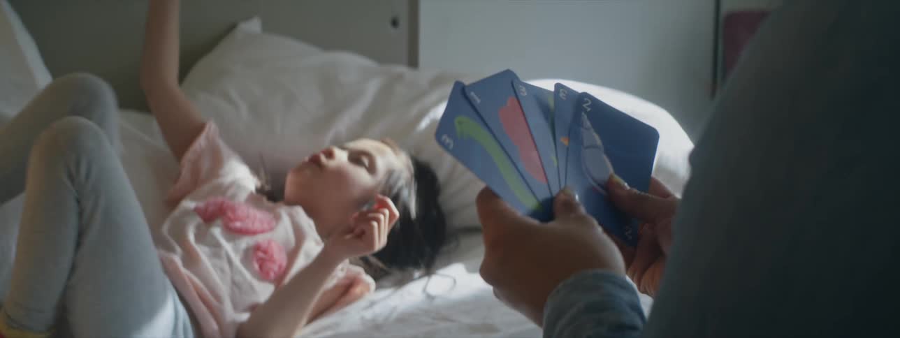 A little girl is sitting on her bed playing cars with her mother
