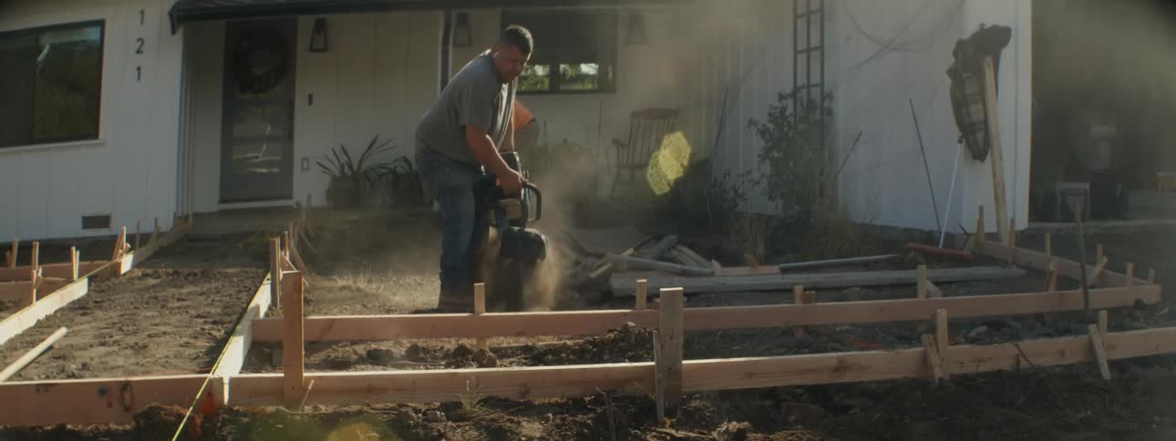 Worker uses chainsaw to cut ground as he and coworker build walkway