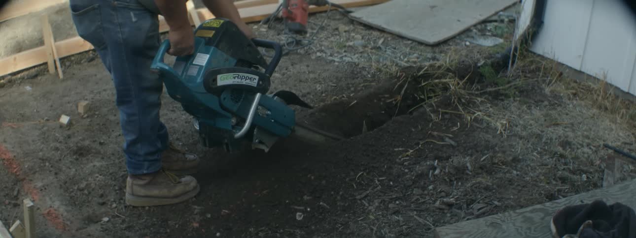 Worker digs trench with a chainsaw near framework for pathway