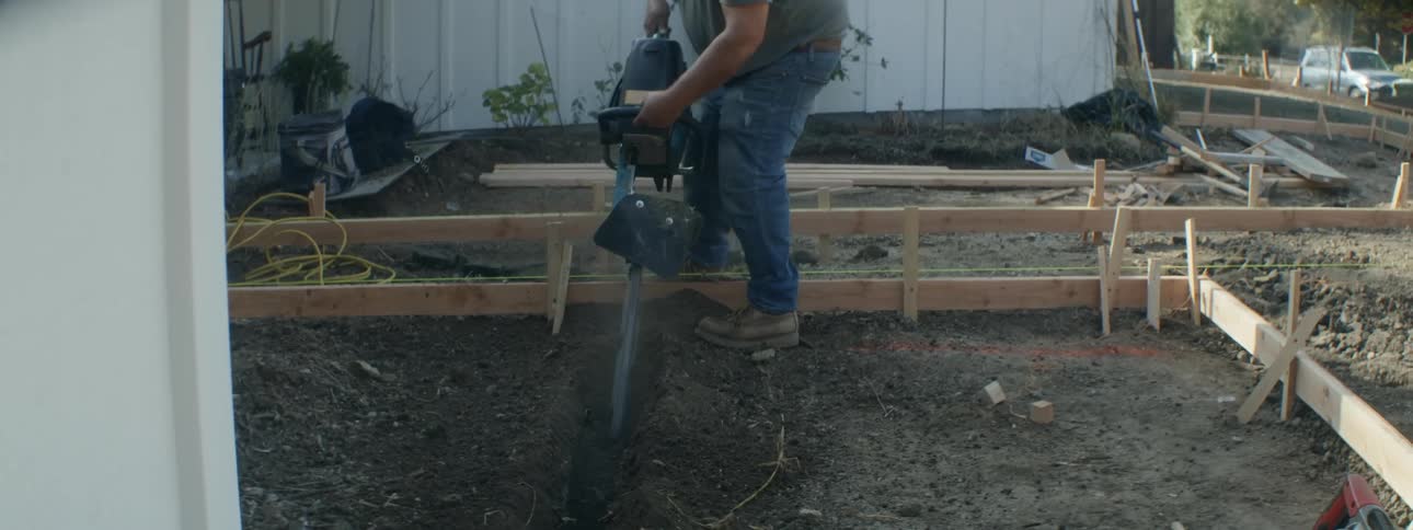Man digs trench with chainsaw while creating framework for path in front yard