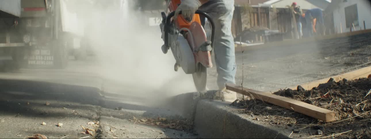 One worker cuts curb with saw as work crew works on putting in driveway