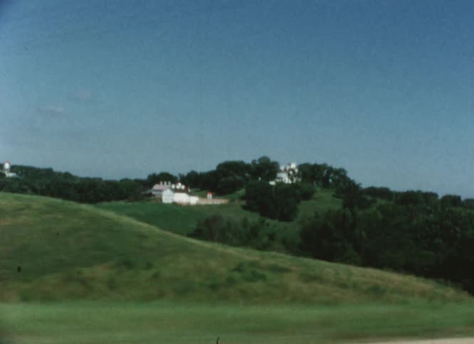 Houses on a hill in the countryside seen from a moving vehicle caught on vintage film