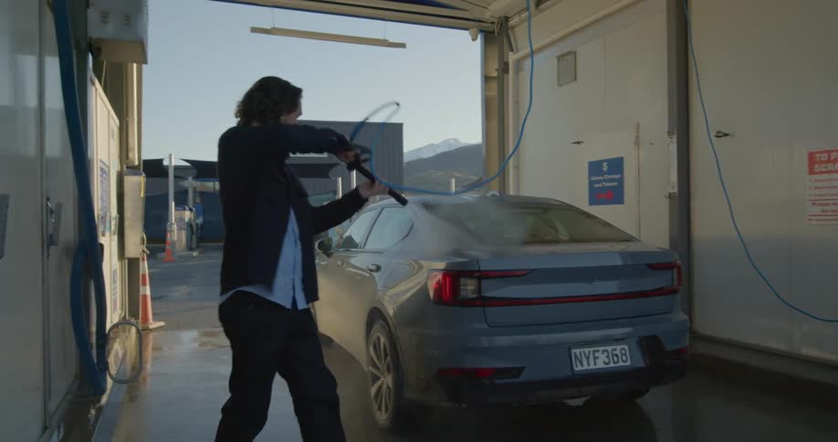 A man is at a car wash holding a hose and washing his car