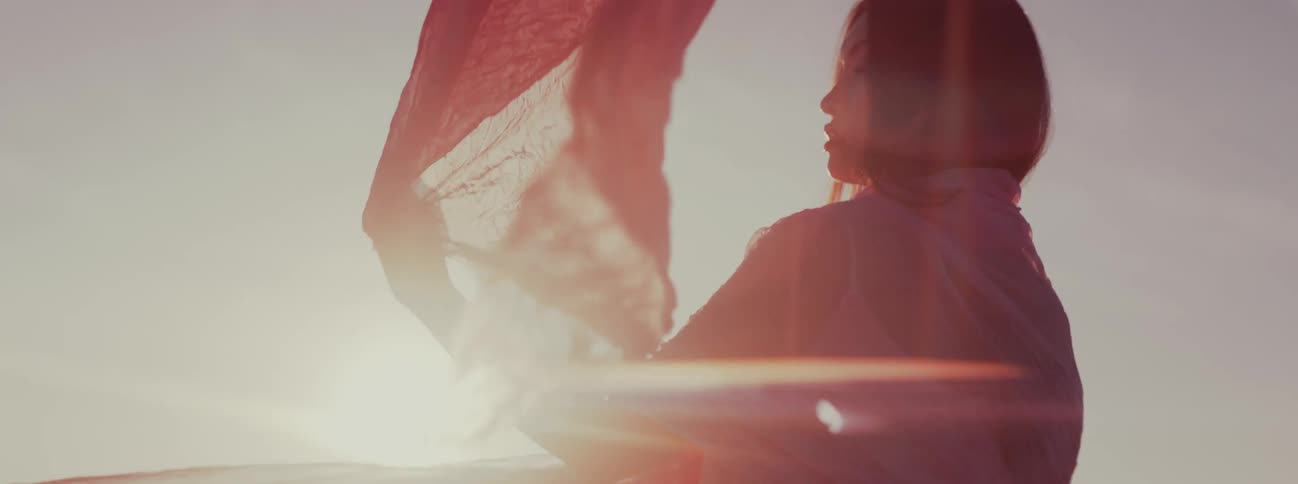 A woman wrapped in a sheer pink veil lets the edge of that veil wave in the wind