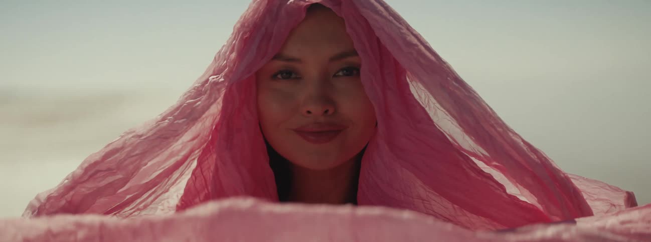 Woman draped in wrap smiles as she lifts fabric to cover her face