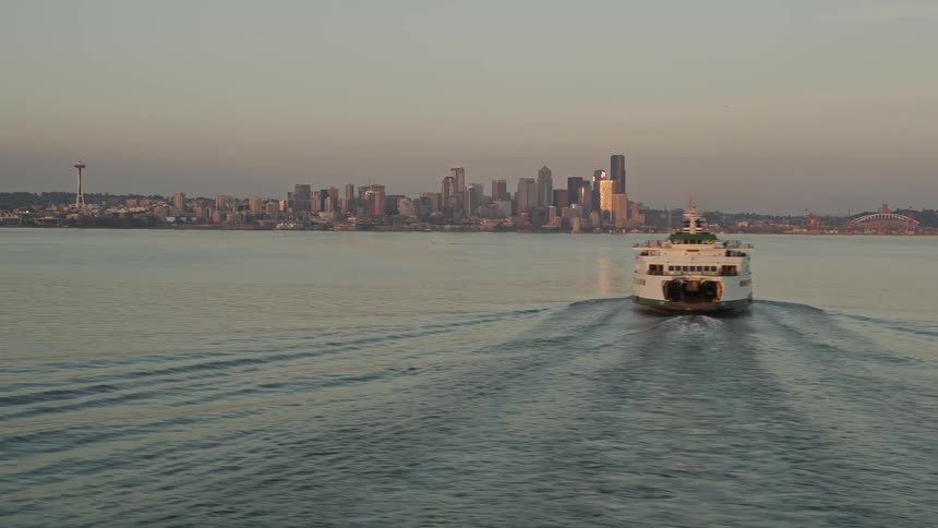 Aerial footage of a ferry sailing in Elliott Bay revealing the stunning Downtown Seattle skyline during sunset