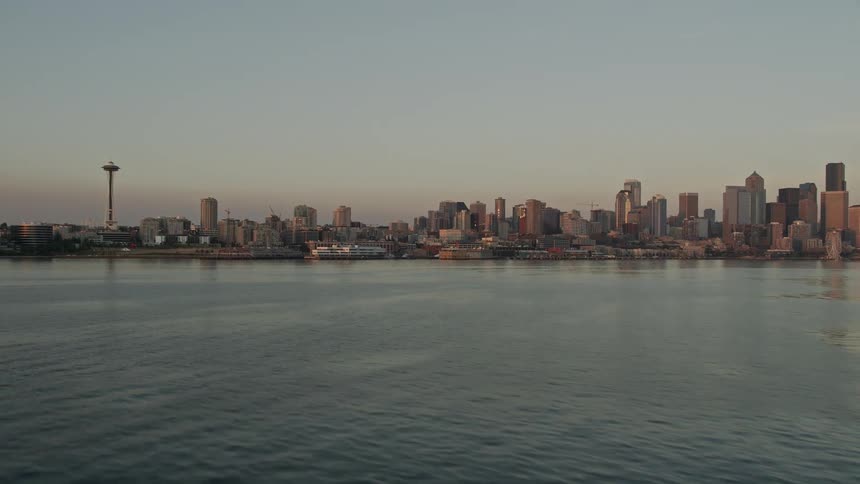 an aerial view of the Seattle skyline and Space Needle at sunset revealing the iconic landmark and bustling downtown area as seen from a low altitude tilt-up shot over Elliott Bay in Washington State