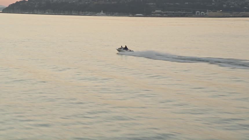 Aerial footage of a speedboat cruising across Elliott Bay at sunset in Seattle Washington creating large waves