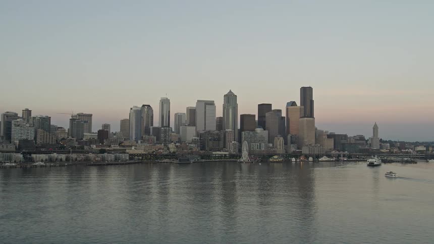 Aerial view of the Central Waterfront and Downtown Seattle skyline at sunset with ferries sailing in Elliott Bay showcasing high rise buildings cityscape and the iconic Ferris Wheel against a partly cloudy sky