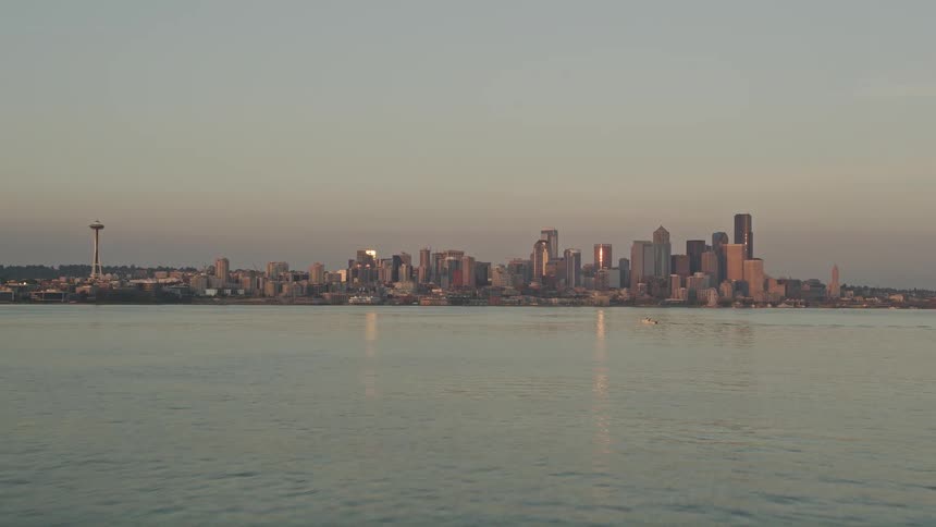 an aerial view of the Downtown Seattle skyline and Space Needle at sunset as the camera tilts up from Elliott Bay showcasing the city's iconic landmarks and high-rise buildings