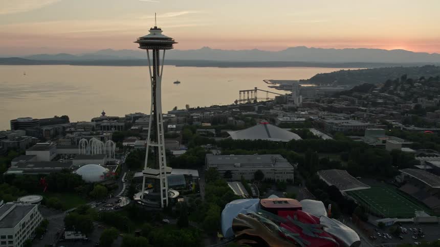 Aerial view of downtown Seattle Washington at sunset as the camera flies over city buildings approaches and orbits KeyArena and the Space Needle