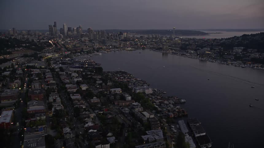 Aerial video of the Ship Canal Bridge approaching Lake Union and the Downtown Seattle skyline at twilight with cloudy skies and light traffic showcasing the high rise metropolis and waterfront nature of the city