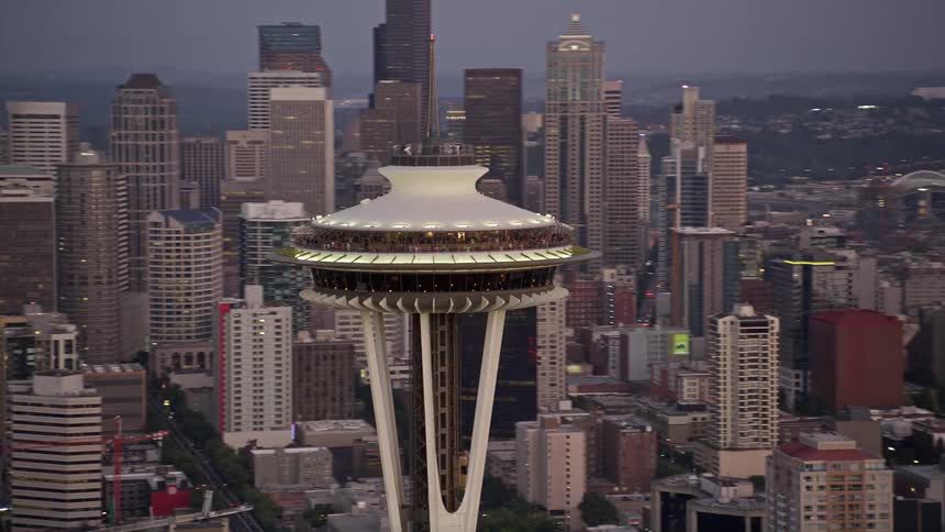 Aerial footage showcasing the iconic Seattle Space Needle as it orbits above the downtown area during a cloudy sunset in Washington offering an sightseeing experience of the city