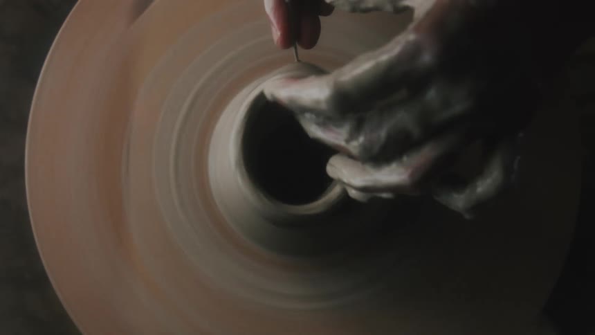 Top down view of a sculptor cutting a piece of fresh clay from a vase on a pottery wheel