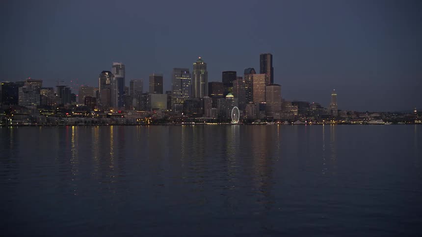  aerial footage captures a low approach to the stunning Downtown Seattle skyline at twilight showcasing the metropolis clear skies high-rise buildings and the iconic Ferris Wheel with the Pacific Northwest's natural beauty and the Puget Sound shoreline in
