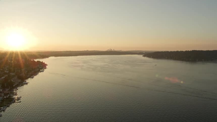 A stunning aerial view of Lake Washington during dusk as the camera flies towards the setting sun revealing homes along the coast