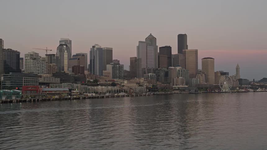 Aerial footage of a low approach to the Great Wheel and Waterfront showcasing the towering skyline of Downtown Seattle at sunset