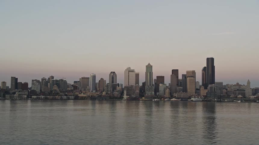 A ferry sails past the downtown Seattle skyline at sunset revealing the bustling metropolis and maritime activity in Elliott Bay