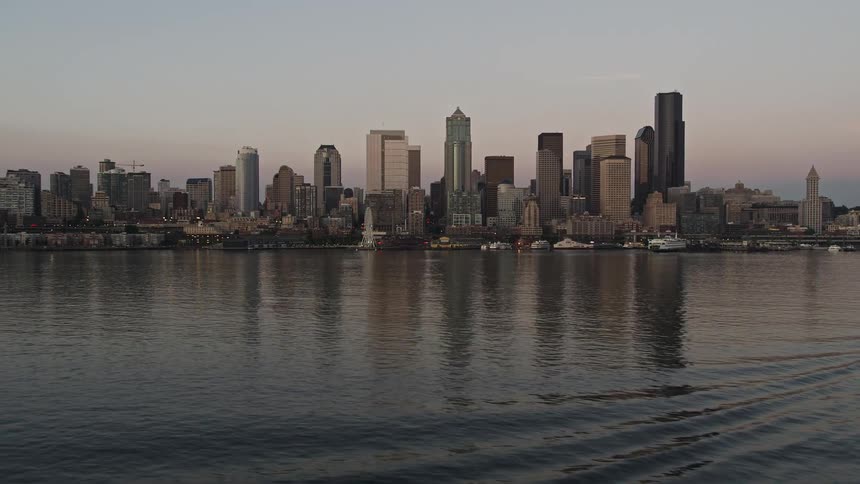 Aerial footage captures a ferry sailing towards the Seattle waterfront and downtown skyline during a mesmerizing sunset in Washington