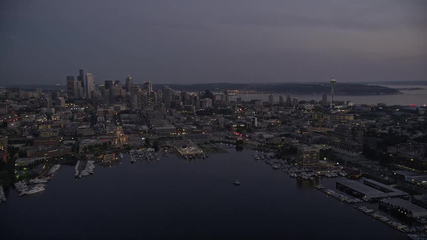 an aerial view of Seattle's iconic Downtown skyline at twilight approaching from the Capitol Hill neighborhood and Lake Union with cloudy skies and the Space Needle in sight