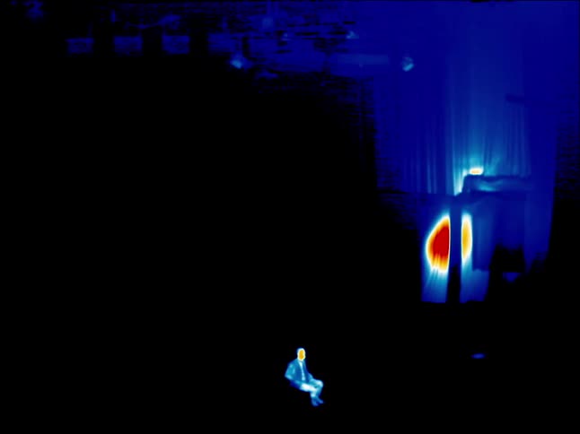 Man sitting on an office chair seen with infrared thermal imagery