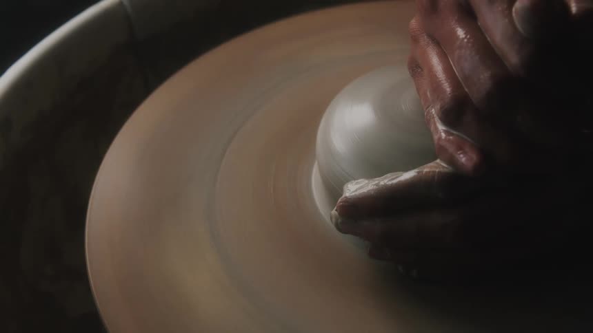 A potter uses their hands to sculpt with clay on a pottery wheel