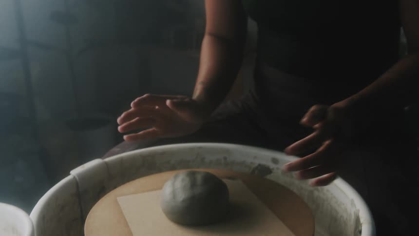 A woman slams clay down on a pottery wheel