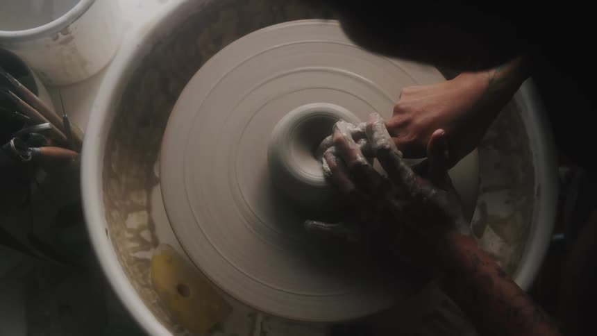 A close up of a person sculpting clay on a spinning wheel