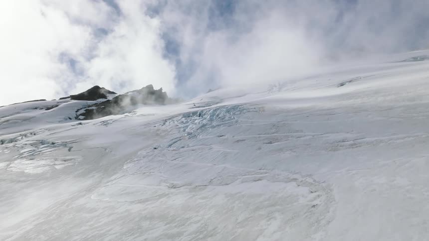 Aerial view of snowy glacier mountain slope against the clouds