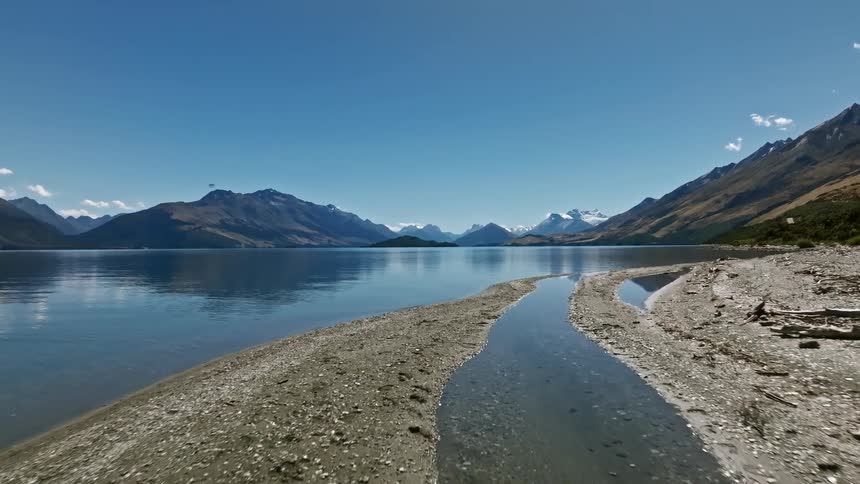 Low level aerial view of beach with clear lake and distant mountains