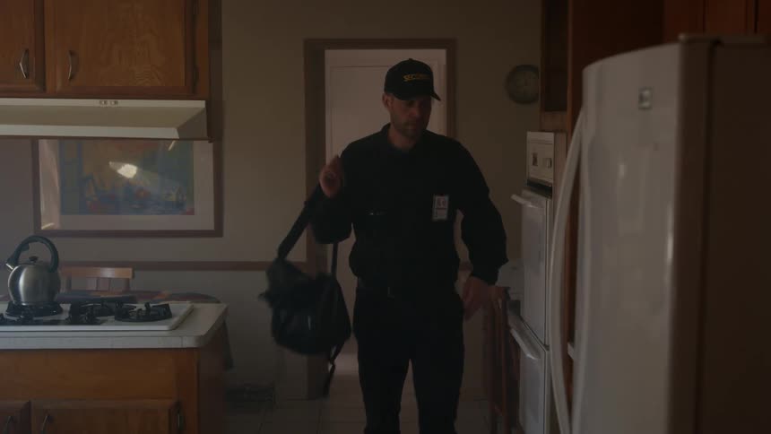 Man wearing id badge walks into kitchen and puts backpack on counter
