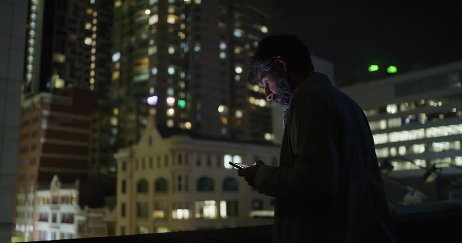 A man is texting on his phone while standing in a downtown city