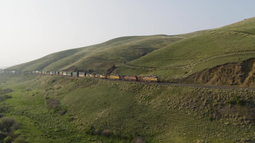 A container train slowly winds its way up a gentle grade along verdant hills