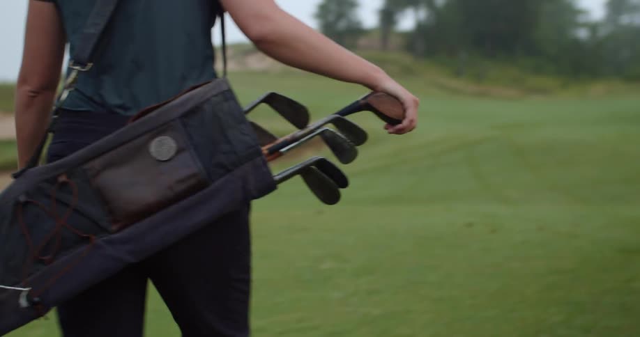 Golfers walks across golf course carrying golf clubs
