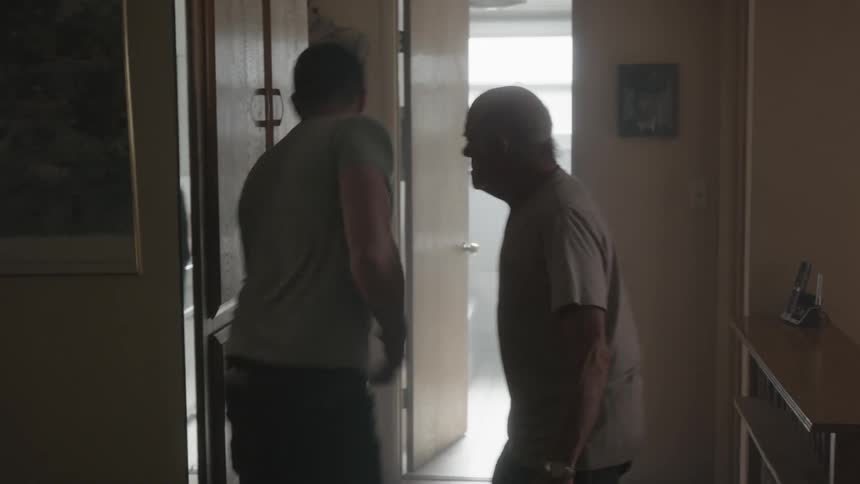 An elderly man and a younger man argue making the younger man fail at putting down a coat on a shelf then picking it up after it falls on the floor as the older man shouts at him