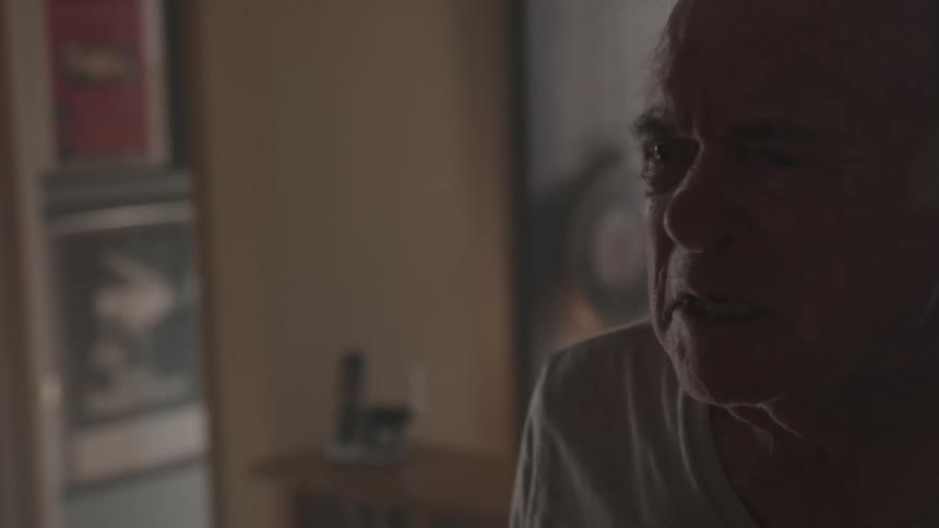 An elderly man yells and gestures while standing in his house