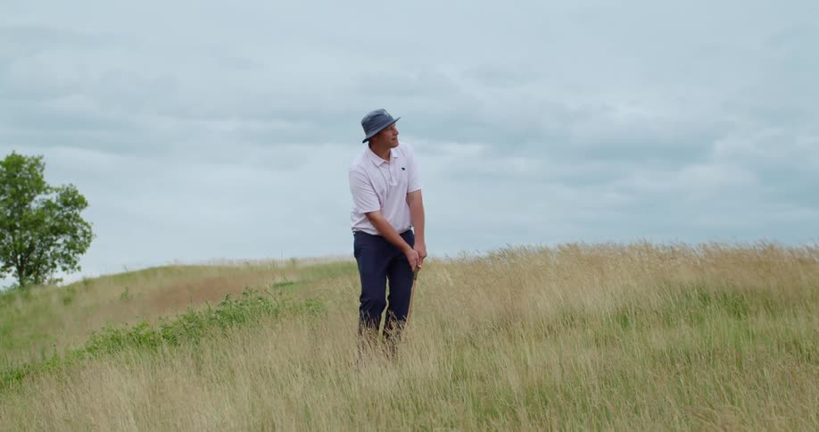 A man hits the golf ball out of the tall grass